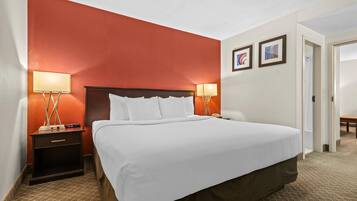 A hotel room with a large bed, two bedside lamps, a nightstand, and a door leading to another room.
