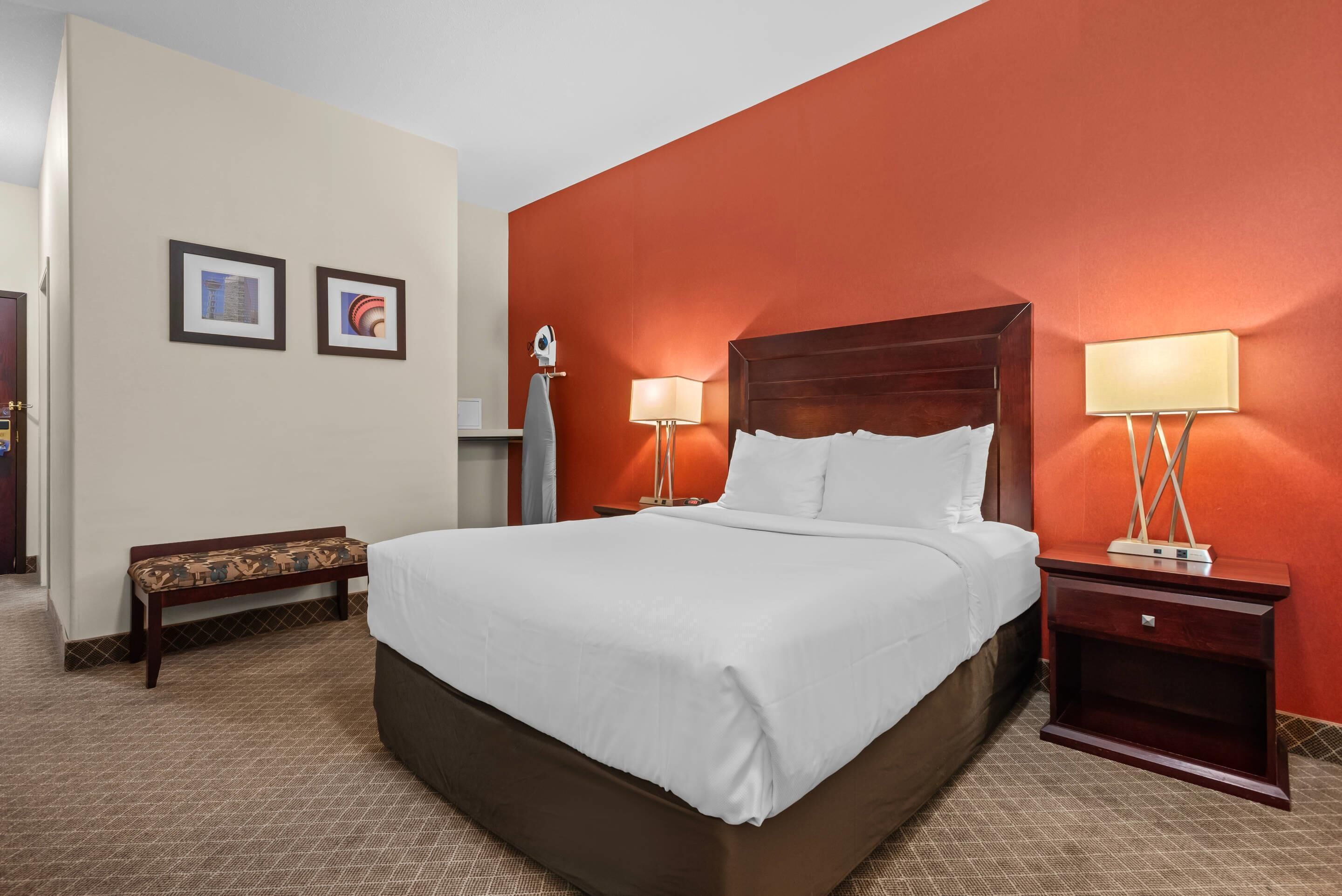 A hotel room with a large bed, two bedside lamps, a bench, and two framed pictures on the wall.