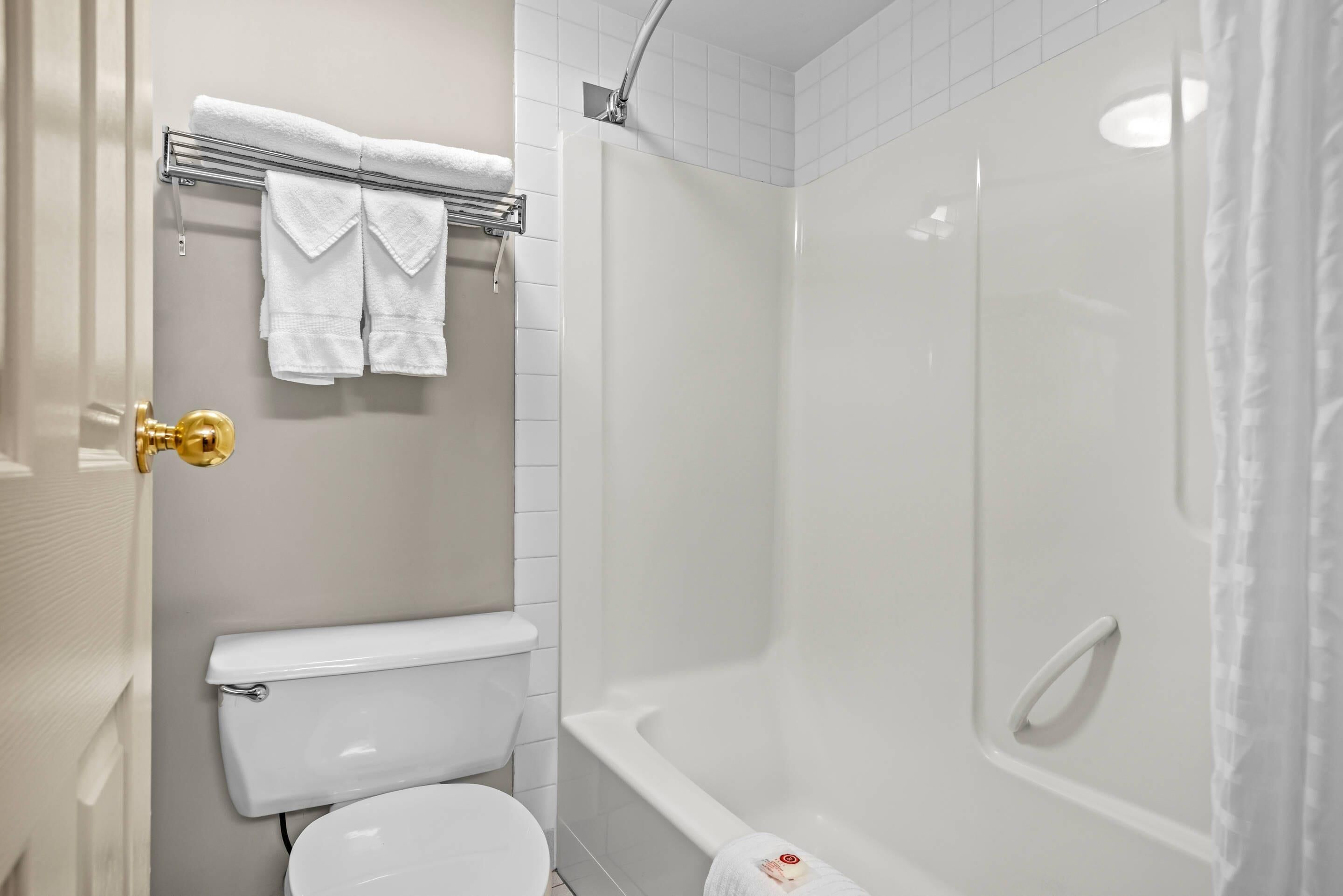 A bathroom with a toilet, a shower, and a towel rack with towels.