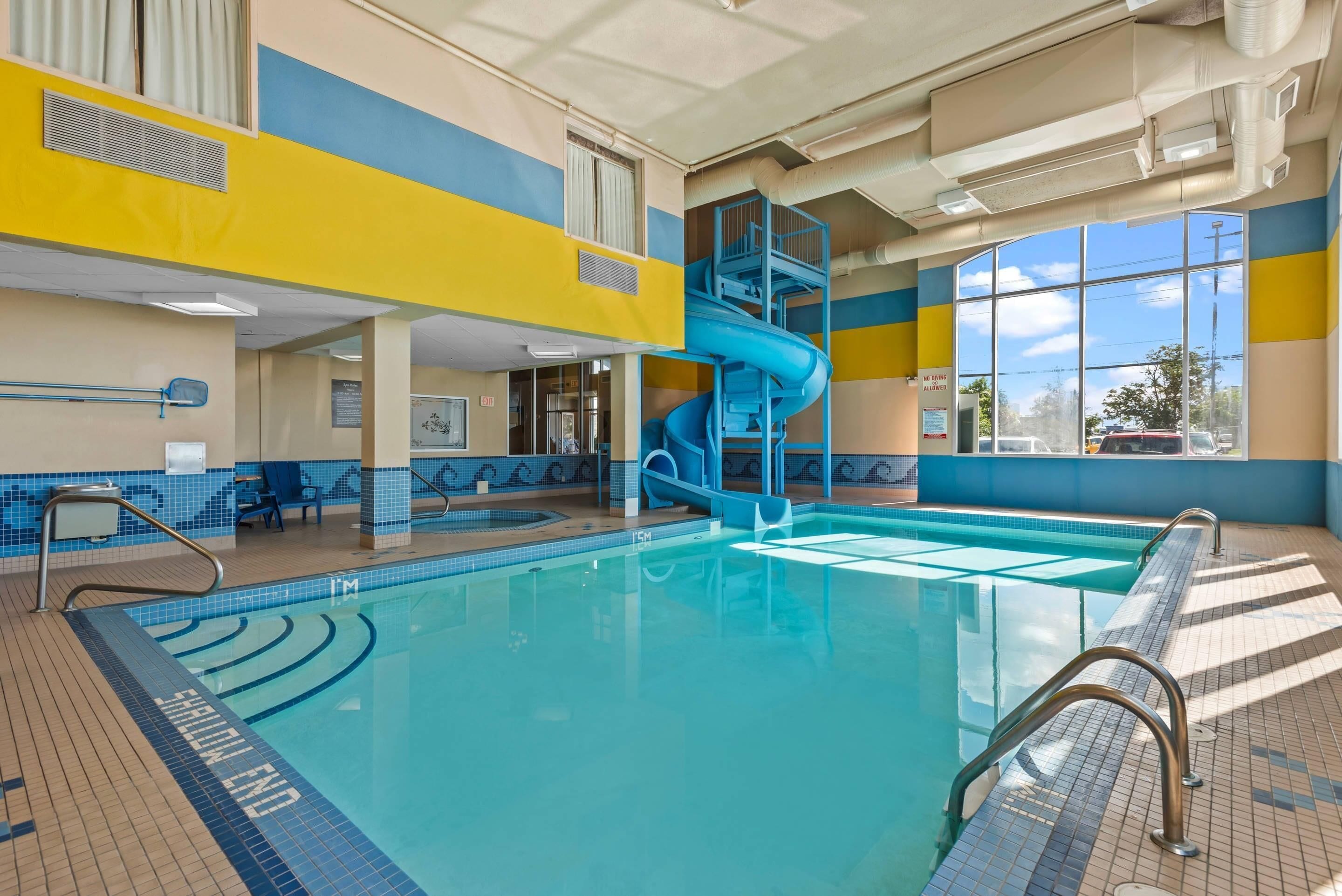 An indoor swimming pool with a blue slide, tiled walls, and a clear view of the outside.