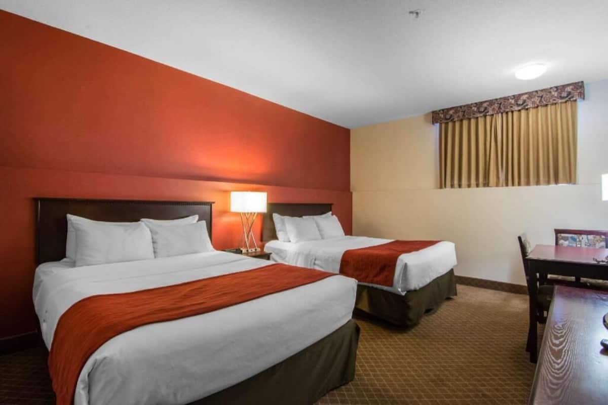 A hotel room with two beds, a desk, and a window with curtains.