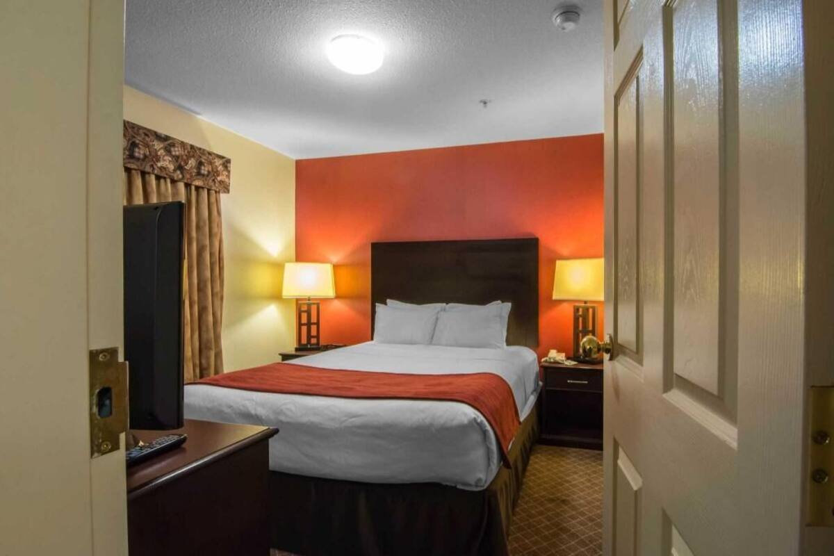 A hotel room with a bed, bedside lamps, a TV, and a desk with a remote control.