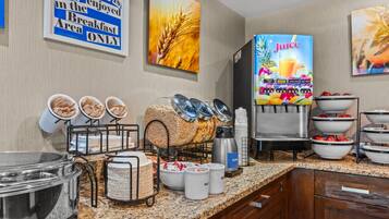 A breakfast buffet area with cereal bowls, a juice dispenser, and a sign indicating breakfast is served in the area only.