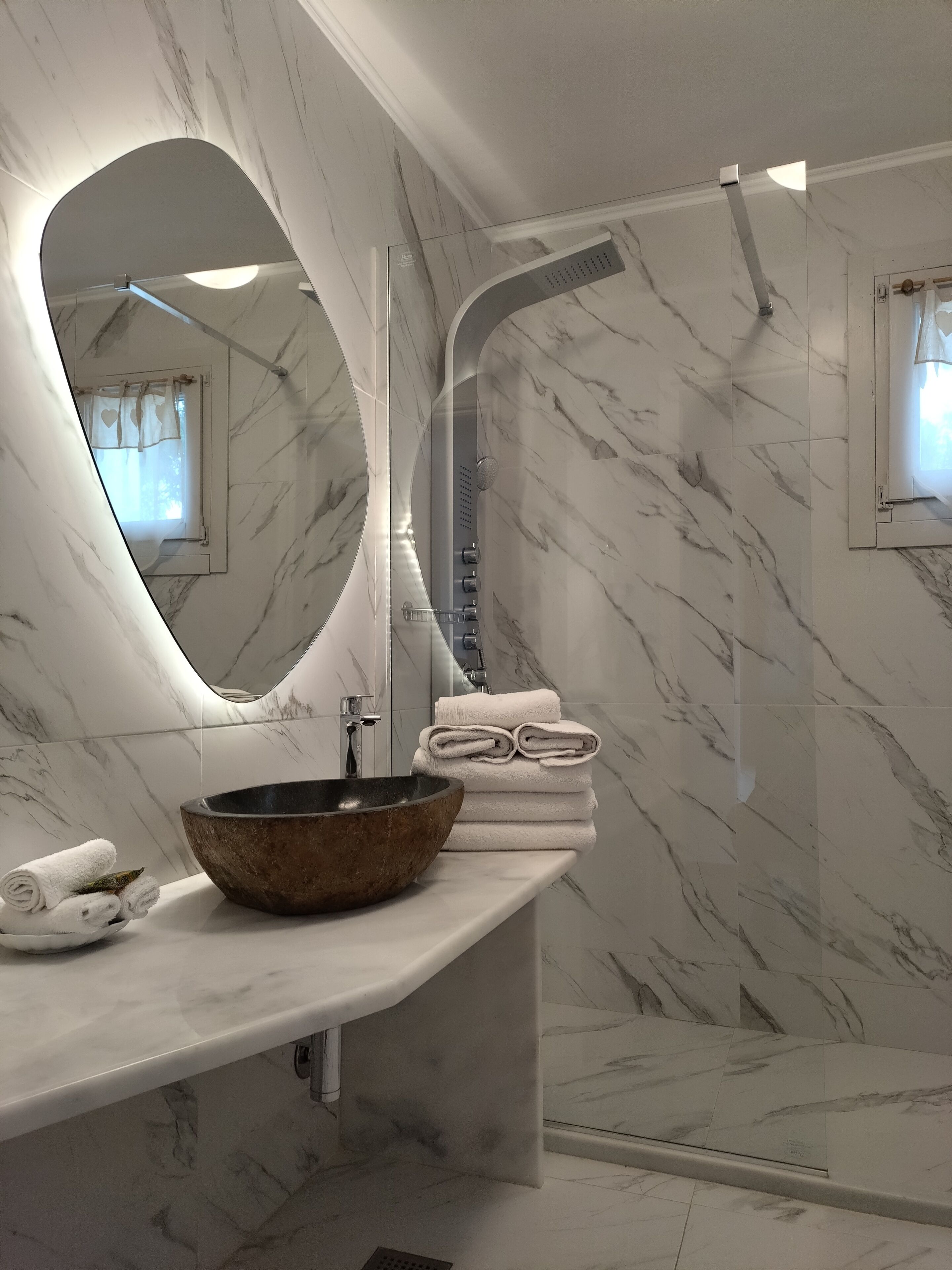 A bathroom with a marble vanity, a large mirror, a vessel sink, and a shower area.