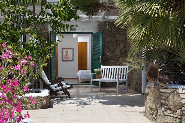 An outdoor seating area with a bench and a chair, a potted plant, and a stone wall. - Tharroe of Mykonos (Mykonos)