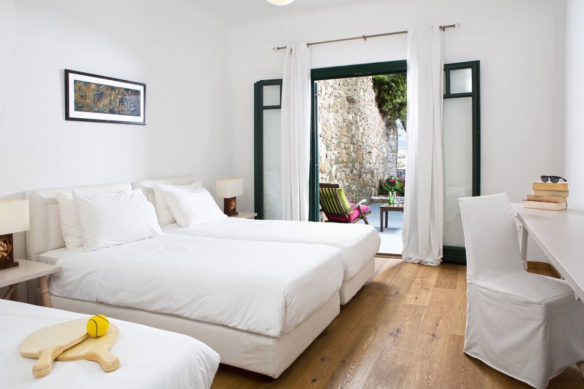 A hotel room with a large bed, a desk, a chair, and a view of the outside.