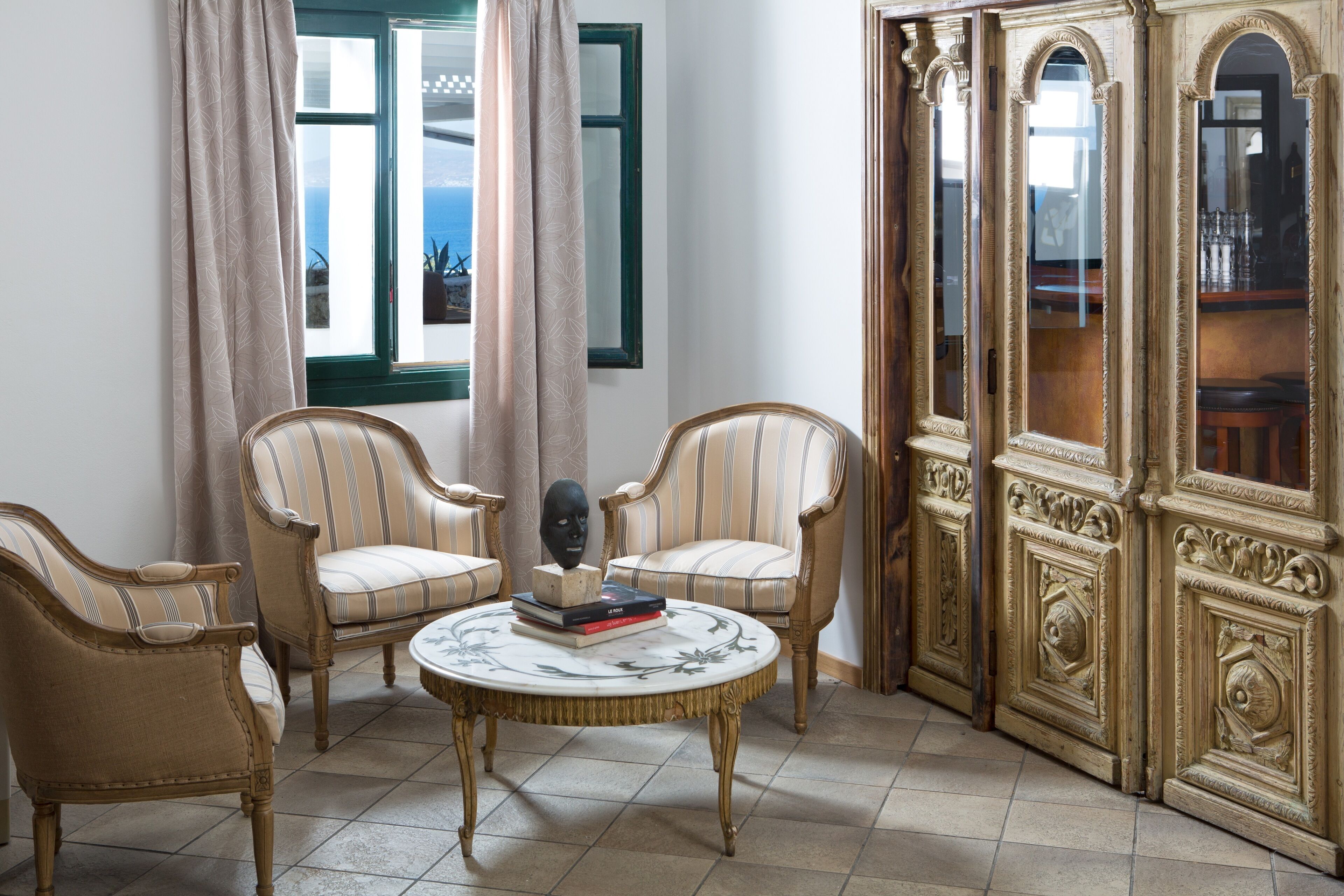 Una habitación con dos sillones tapizados, una mesa redonda con tablero decorativo y un espejo grande y ornamentado.