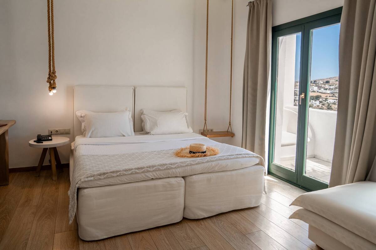 A bedroom with a large bed, a bedside table, a hanging light, and a view of the outside through a sliding door.