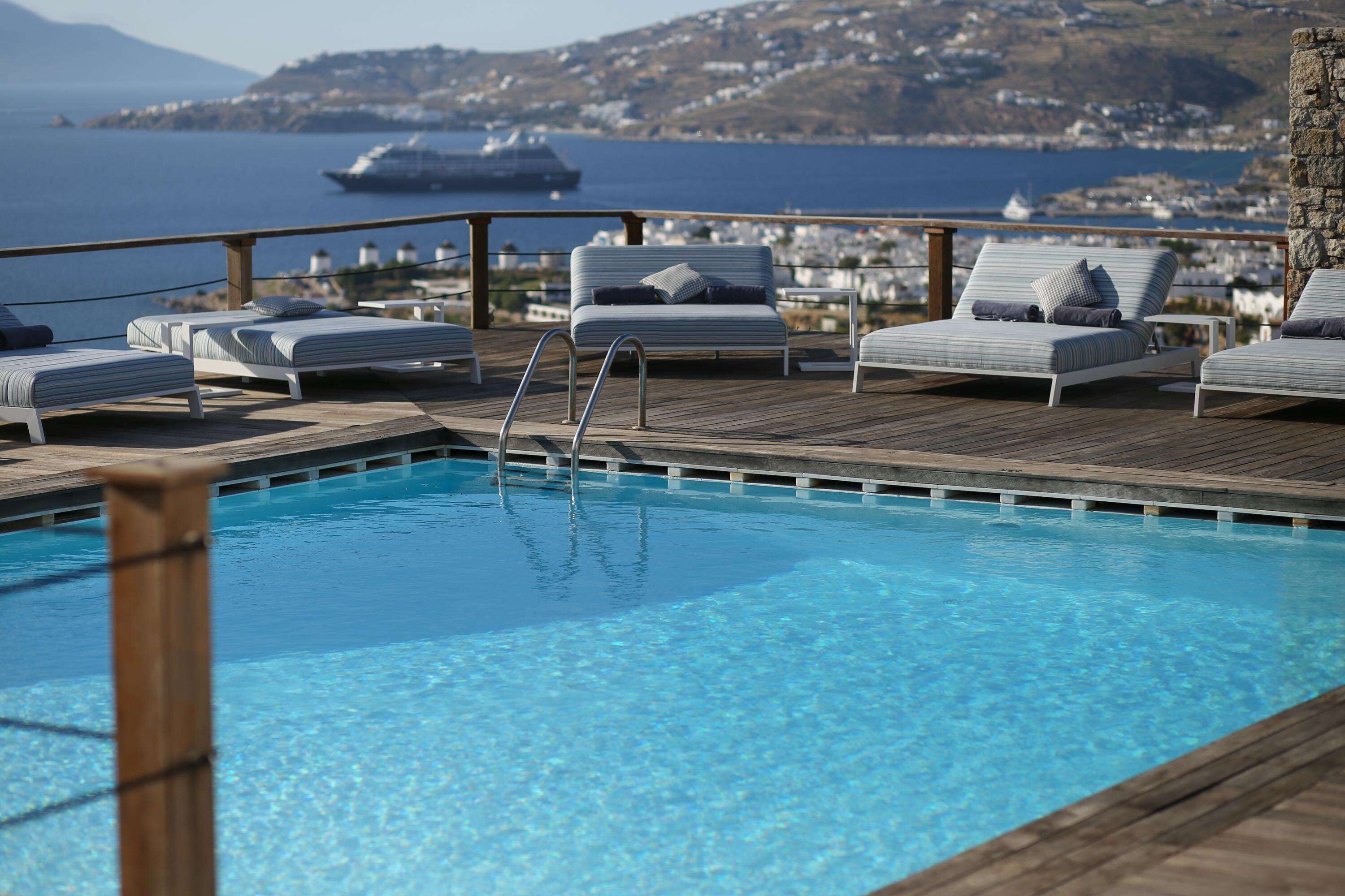Zona de piscina con sillones de descanso y vista al mar, con un crucero al fondo.