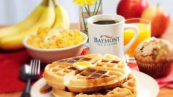 A breakfast setting with waffles, a muffin, a bowl of cereal, a cup of coffee, bananas, apples, and a glass of orange juice.