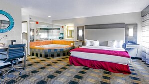 A hotel room with a large bed, a desk, a chair, a bathtub, and a mirror. - Baymont by Wyndham Jackson (Jackson)