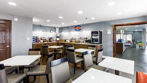 A modern restaurant with white tables and chairs, a kitchen area, and a clock on the wall. - Baymont by Wyndham Jackson (Jackson)