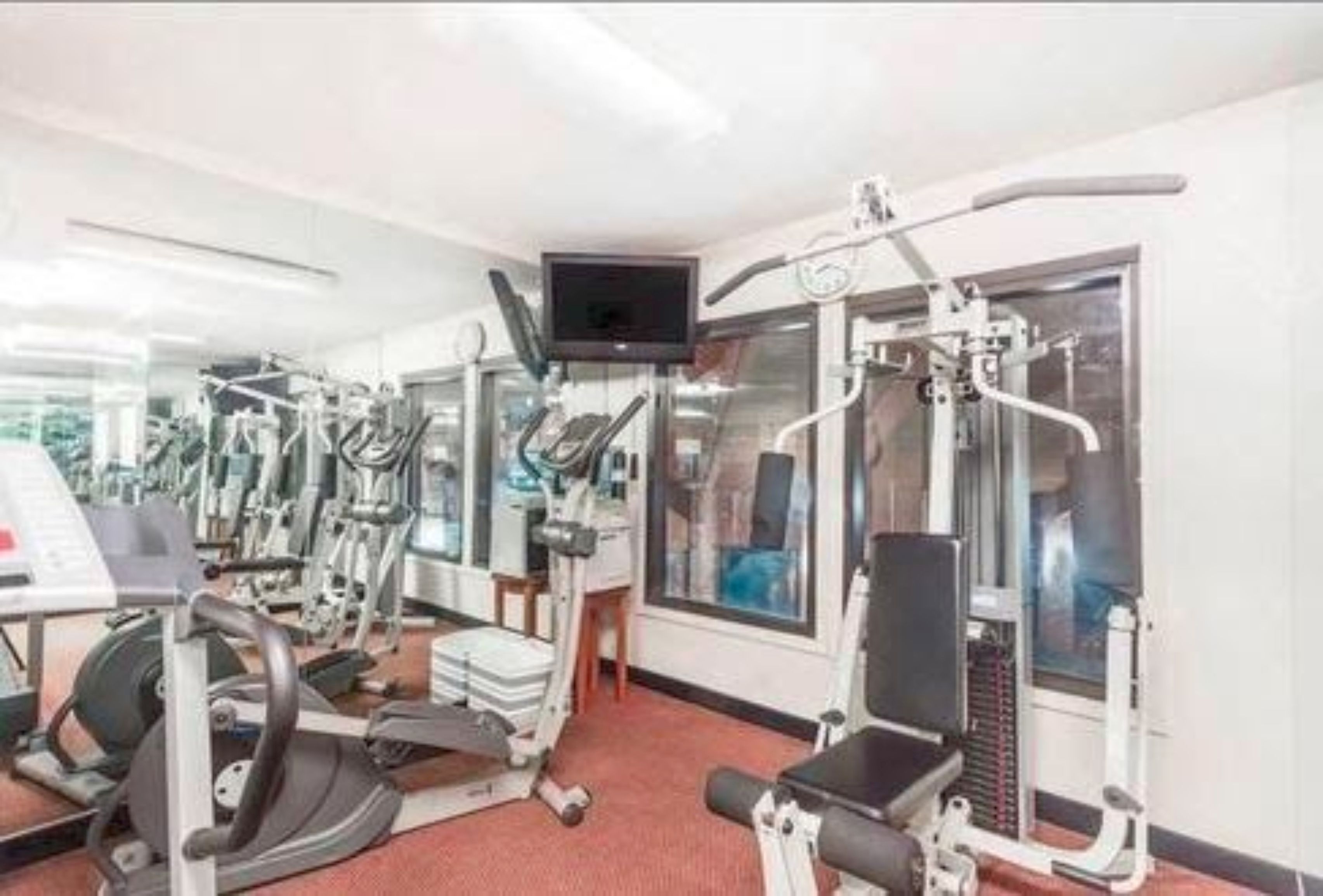 A gym with various exercise machines, a television, and large windows.