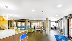 A hotel reception area with a wooden reception desk, a blue carpet with the hotel name, a seating area with a sofa and chairs, and a large window providing a view of the outdoors. - Baymont by Wyndham Jackson (Jackson)