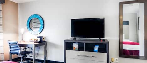 A hotel room with a bed, a desk with a chair, a television, a dresser, a mirror, and a window.