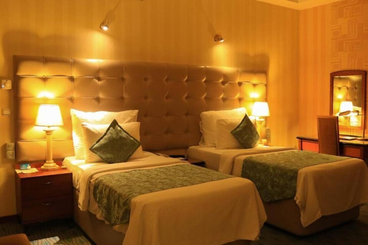 A hotel room with two beds, each with a headboard, bedside lamps, and a mirror on the wall.