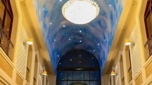 Eine prachtvolle Eingangshalle mit hoher Decke, einem zentralen Kronleuchter und einer Glastür am Ende.