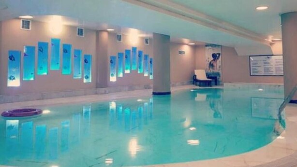 Ein Hallenbad mit klarem Wasser, einem Rettungsschwimmerstuhl und Wandleuchten.