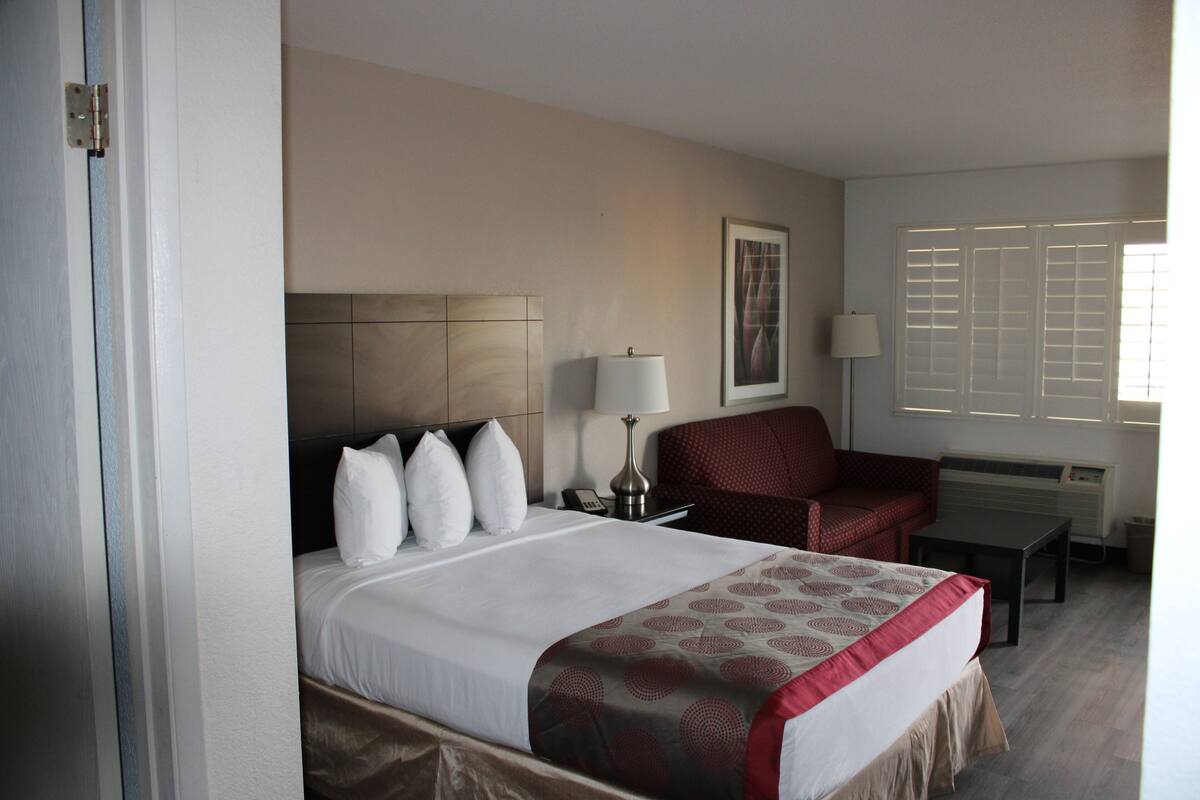 A hotel room with a bed, a chair, a table, and a lamp.