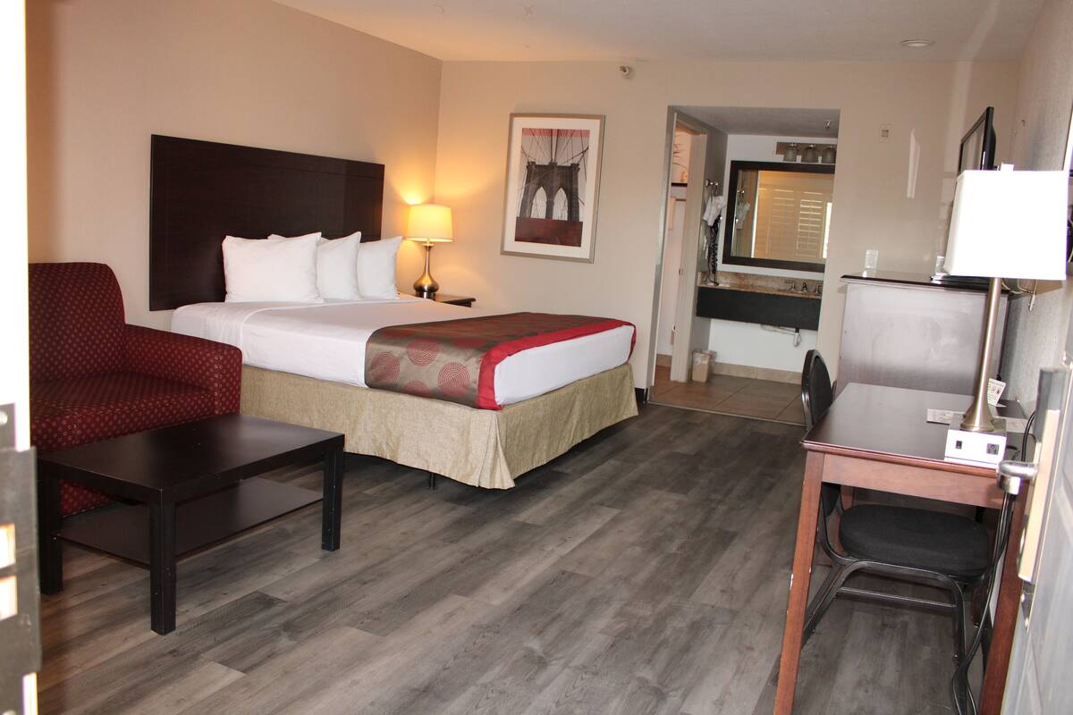 A hotel room with a bed, a desk, a chair, a lamp, and a painting on the wall.