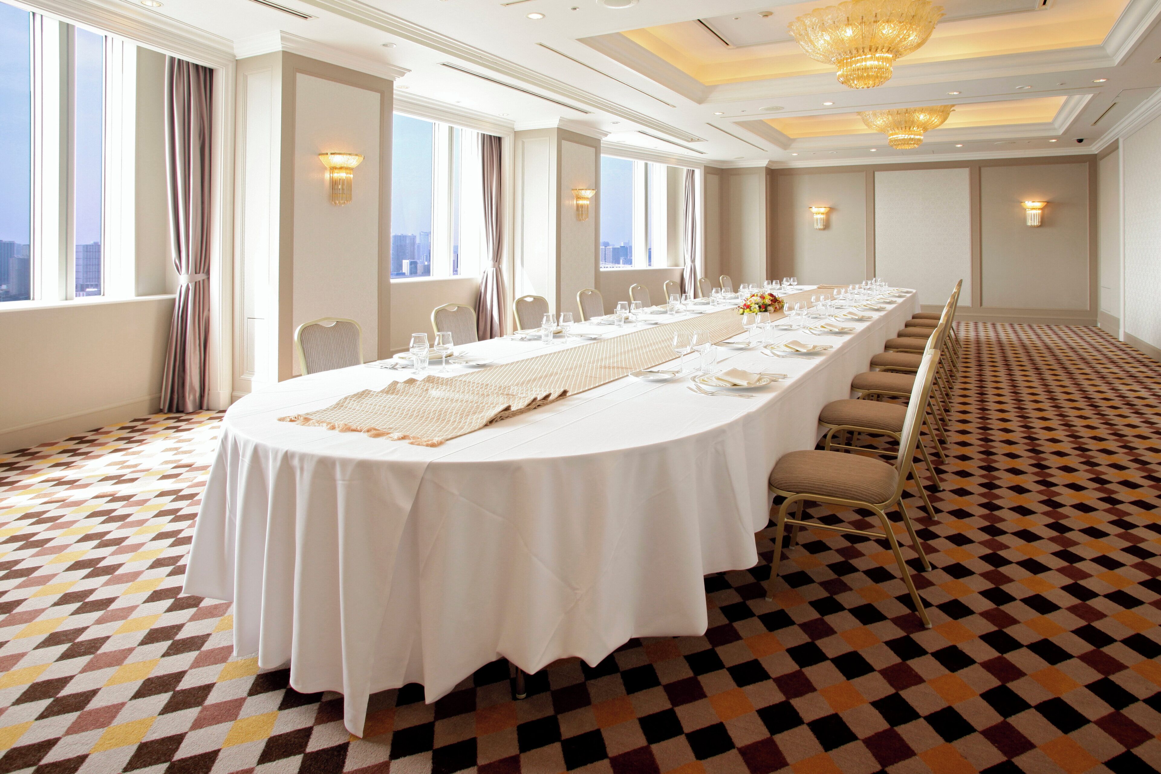 A conference room with a long table set for a meeting, large windows, and a patterned floor.