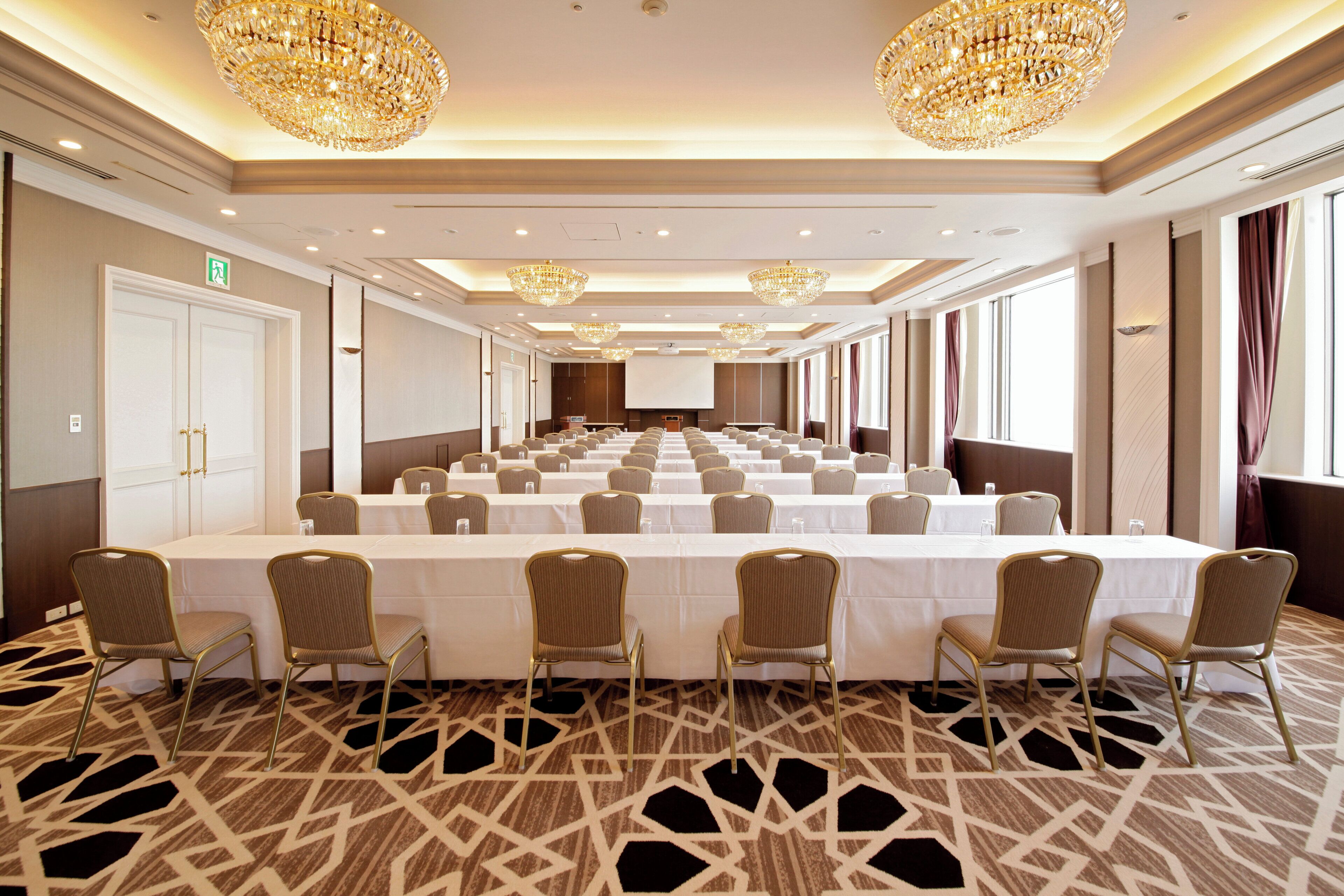 Un salón de conferencias con una larga mesa, sillas, candelabros y una pantalla de proyector.