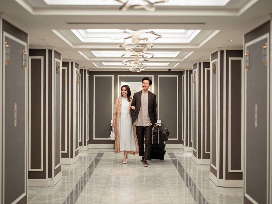 A modern hotel corridor with a reflective floor, symmetrical wall paneling, and a central light fixture.