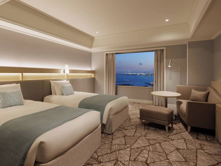 A hotel room with two beds, a small table, a sofa, and a view of the water.