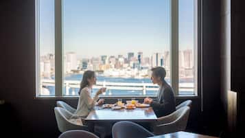 A dining area with a table set for two, large windows offering a city view.
