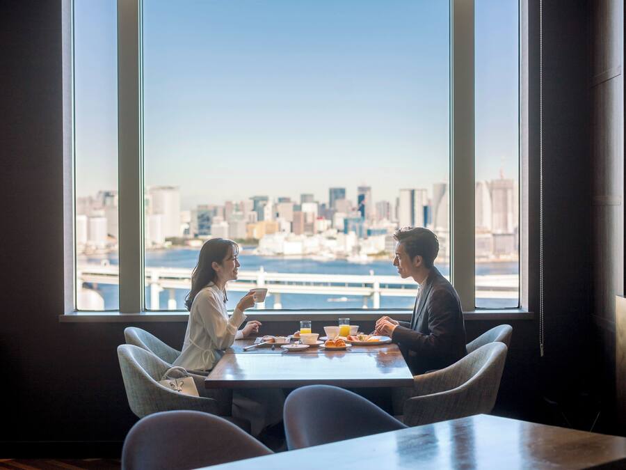 Ein Essbereich mit Tisch für zwei Personen, große Fenster mit Blick auf die Stadt.