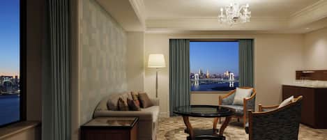 A hotel room with a sofa, armchairs, a table, a view of a cityscape, and a chandelier.