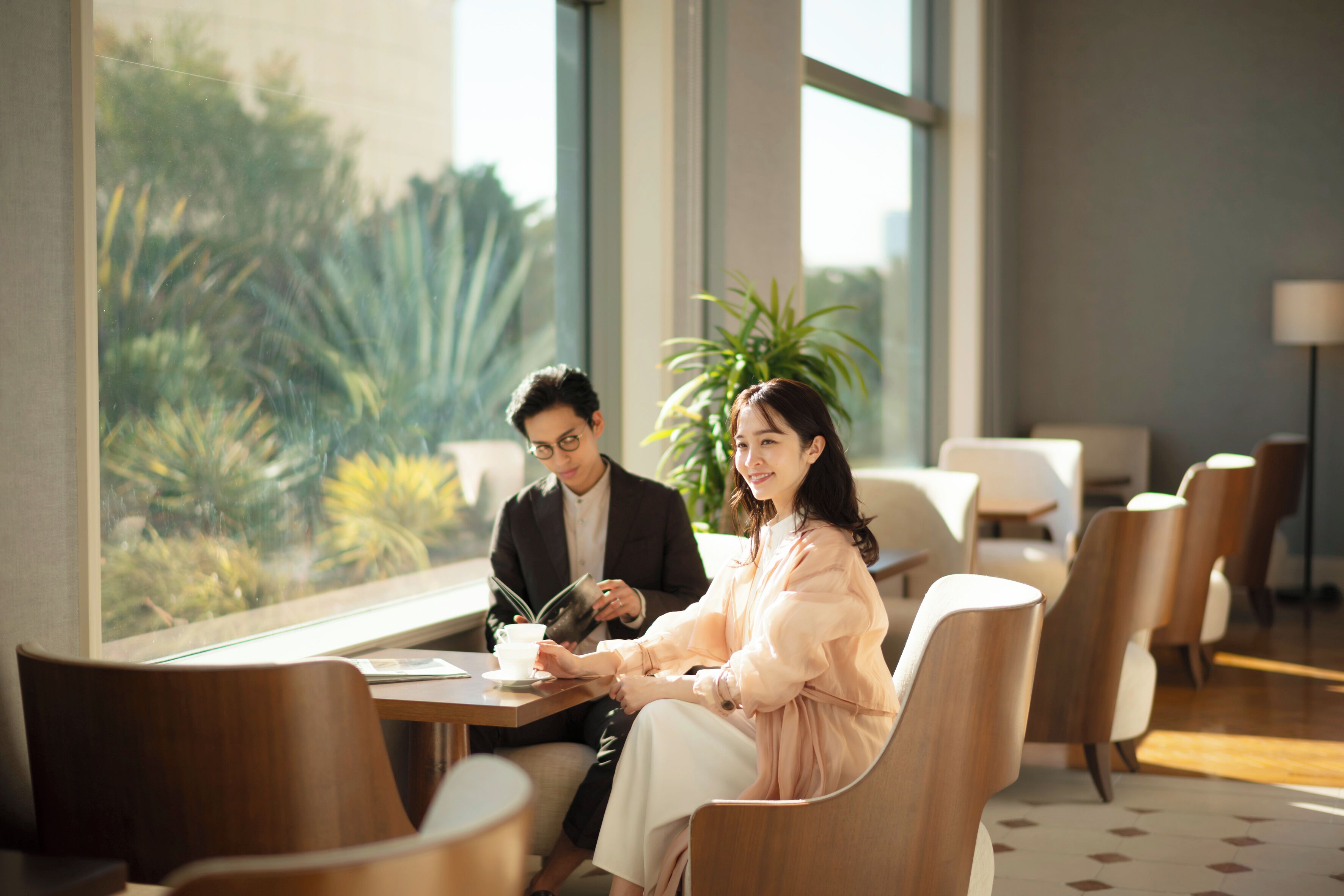 A modern conference room with a large window, a table with a cup and a book, and several chairs.