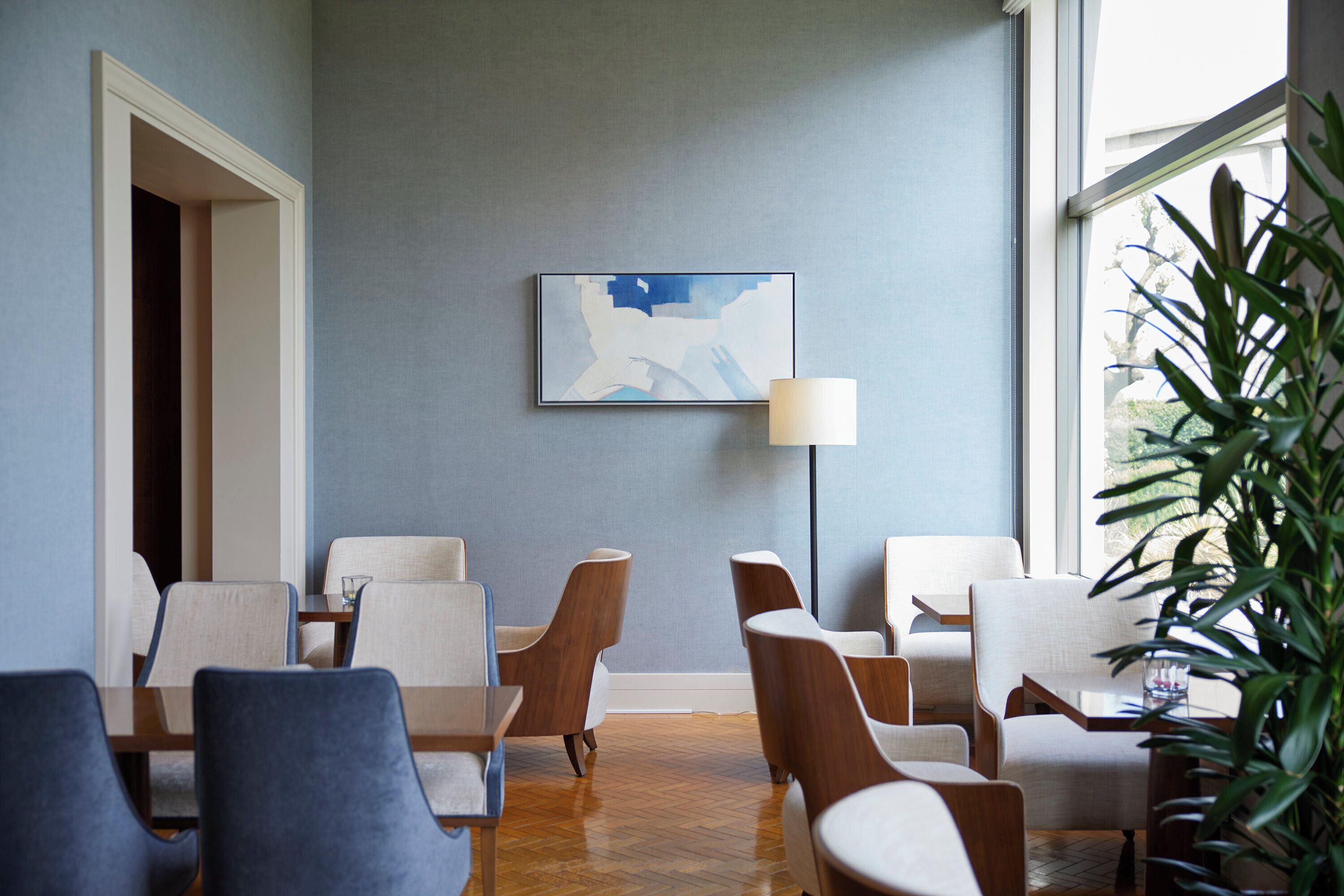 A modern hotel lobby with a blue wall, a framed abstract painting, and a large window with a view of greenery.