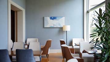 A modern hotel lobby with a blue wall, a framed abstract painting, and a large window with a view of greenery.