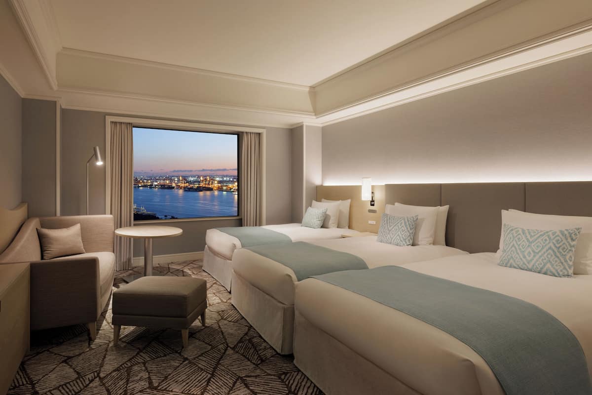 A hotel room with two beds, a sofa, a small table, and a view of a cityscape.