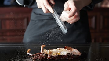 Una persona rallando una sustancia blanca, probablemente queso, sobre un langostino sobre una superficie negra.