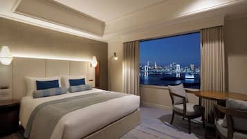 Quarto de hotel com uma cama grande, uma escrivaninha e vista para a cidade à noite.