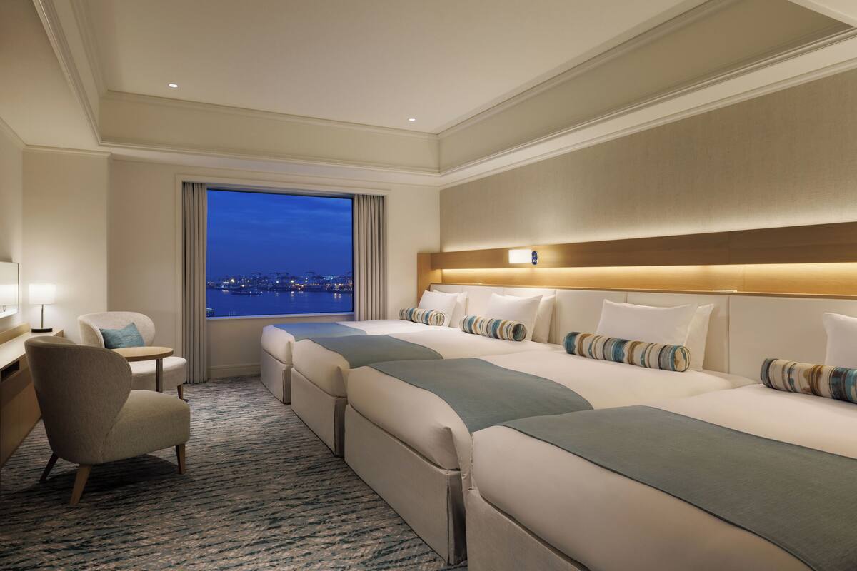 A hotel room with a large bed, a desk, a chair, and a view of the city at night.