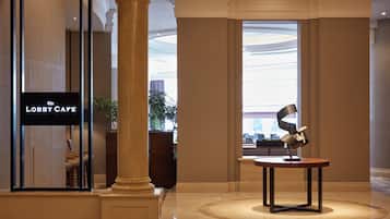 A lobby with a 'Lobbi Cafe' sign, a large column, a modern sculpture, and a view of the street through large windows.