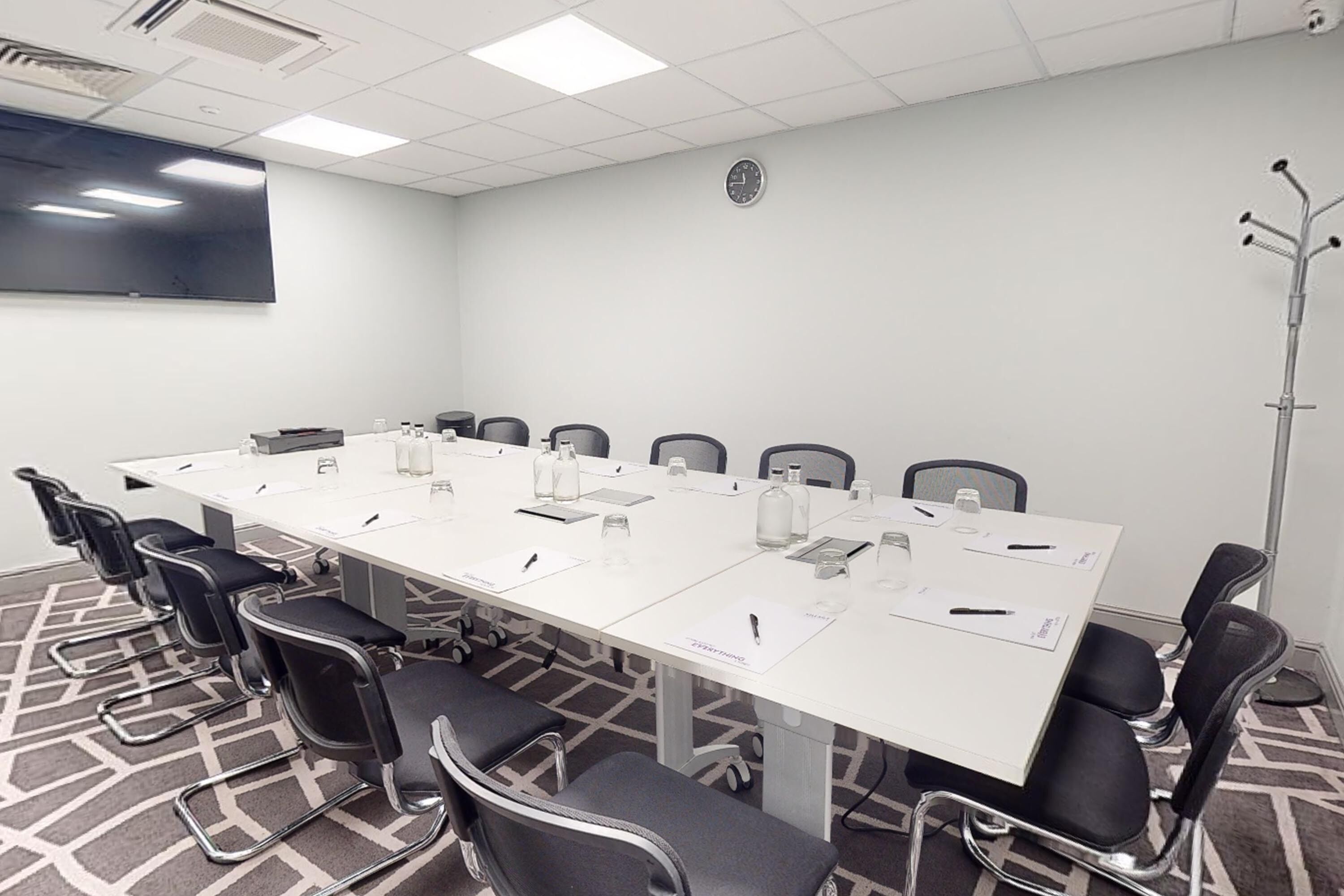 A conference room with a long table, black chairs, a flat-screen TV, and a clock on the wall.