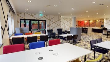 Un moderno vestíbulo de hotel con varias zonas de estar, incluyendo mesas y sillas, y una recepción visible.