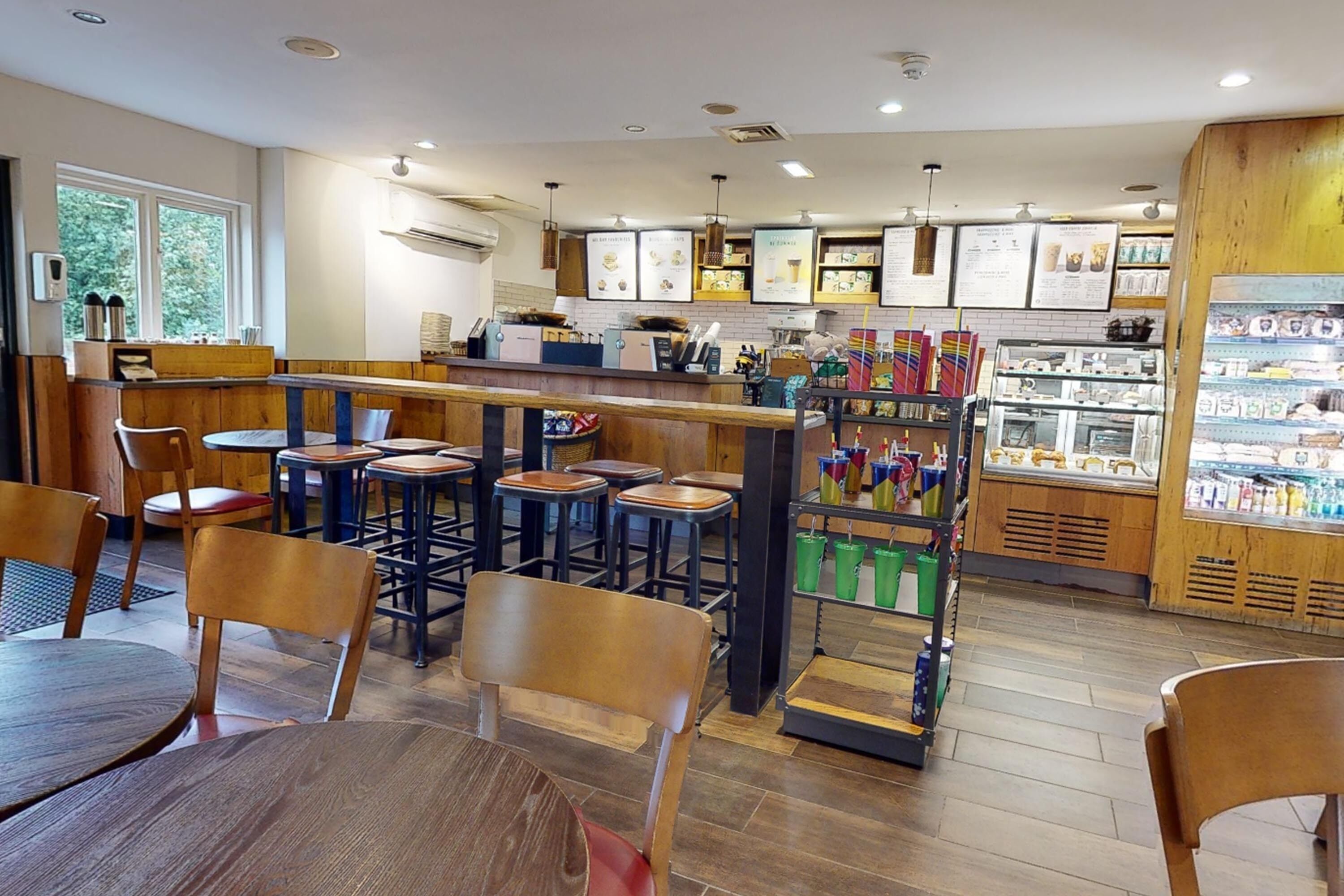 A café with wooden tables and chairs, a counter with a menu, and a refrigerated display case.