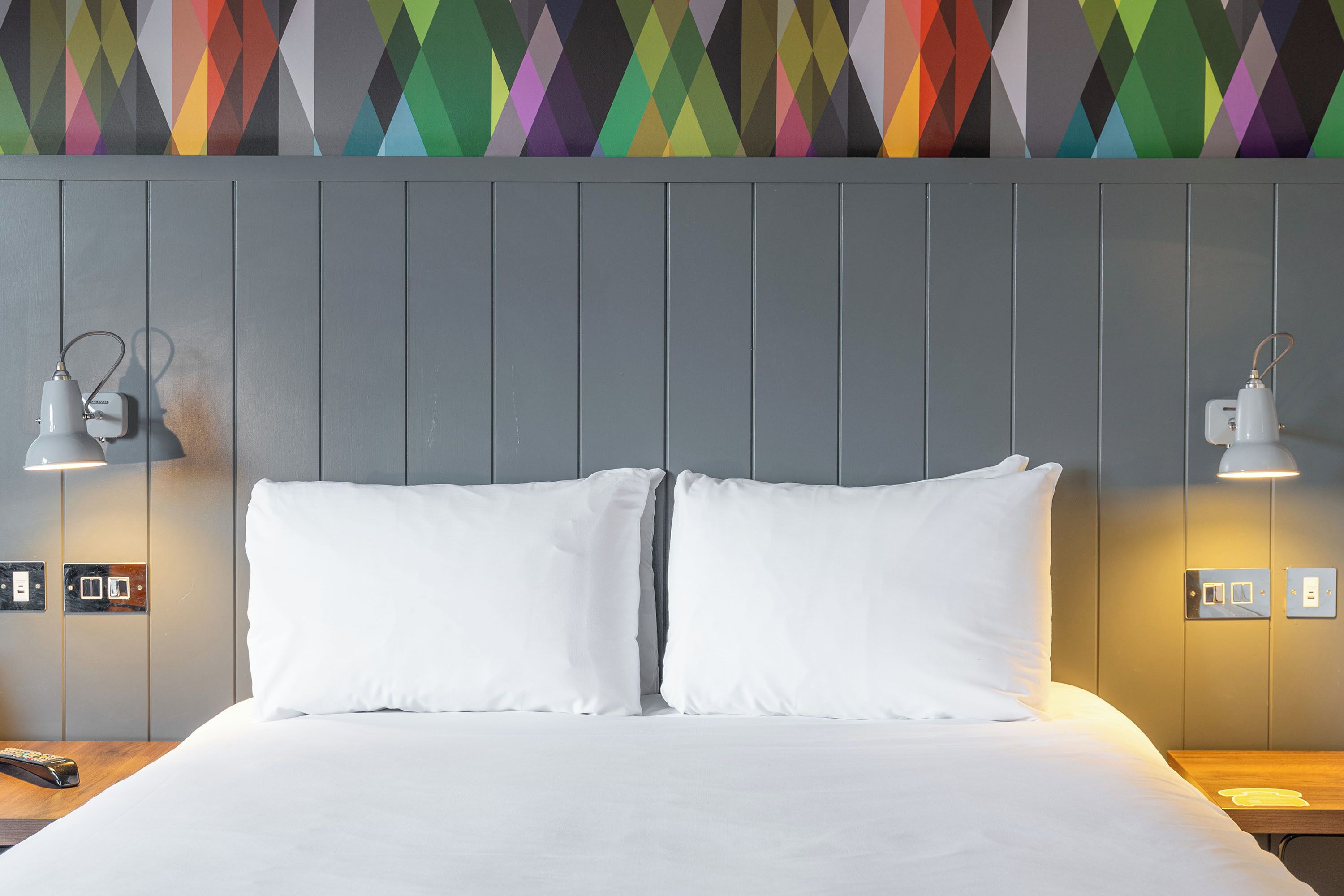A neatly made bed with white linens, two bedside lamps, and a wall with a geometric patterned design.