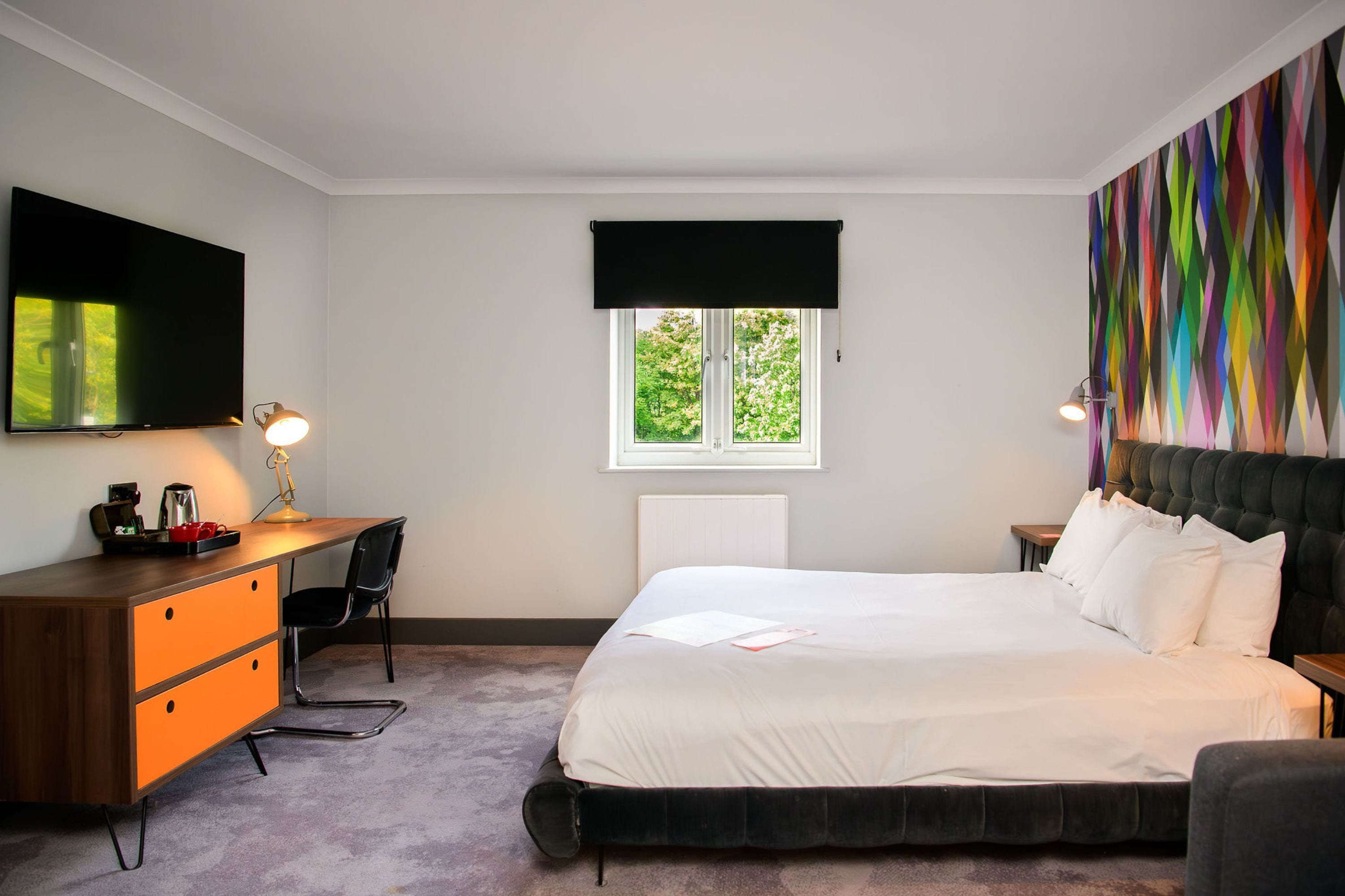 Habitación de hotel con cama, escritorio con silla, televisión y ventana con vistas a zonas verdes.