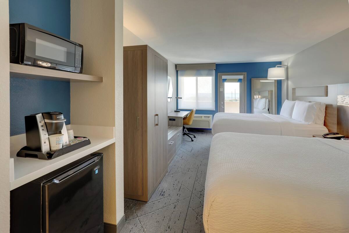 A hotel room with a bed, a desk, a microwave, a coffee maker, and a mini-fridge.