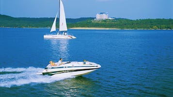 A speedboat on a lake with a sailboat in the background and a building on a hill.