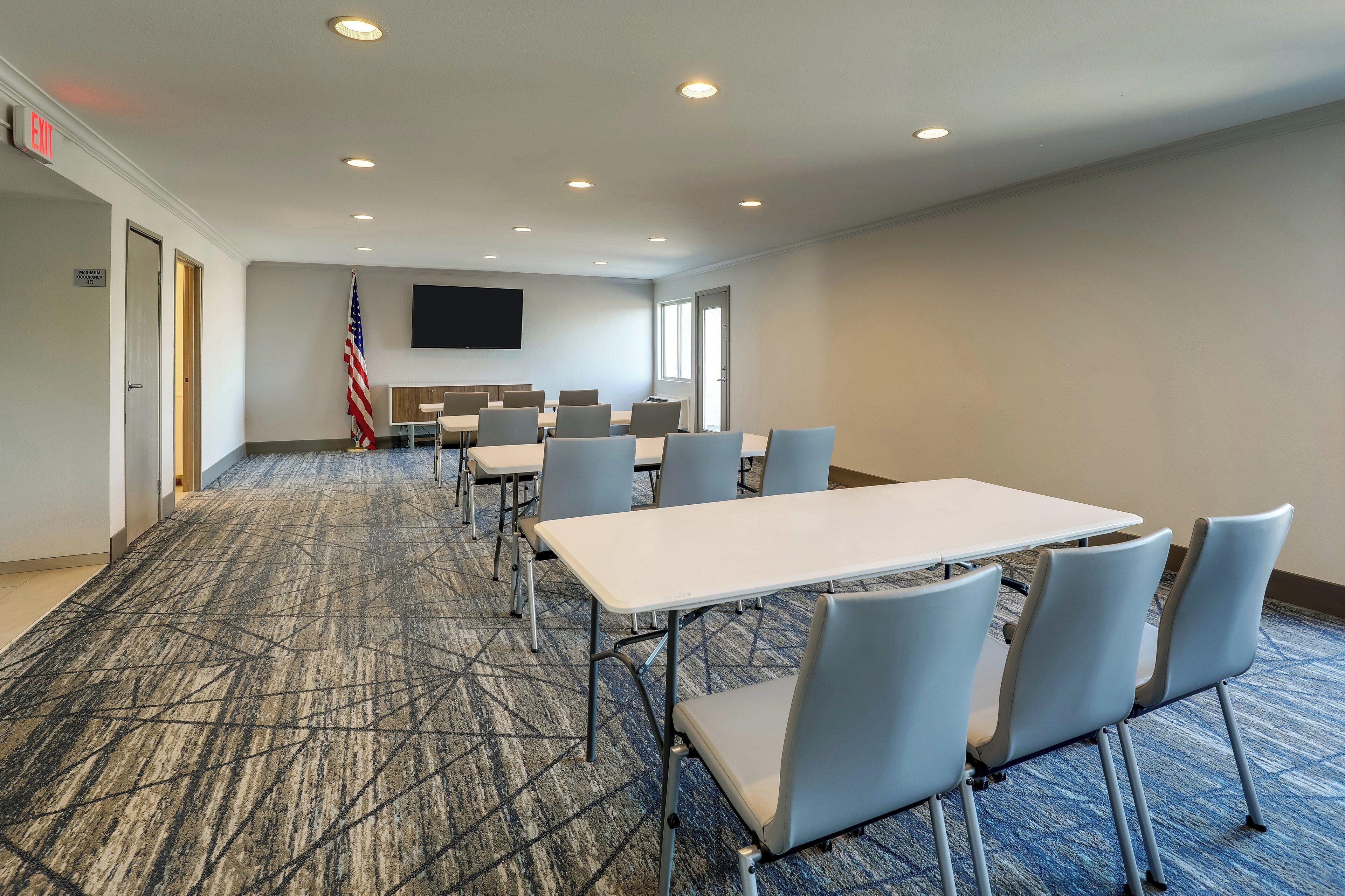 A conference room with a carpeted floor, white tables, and grey chairs.