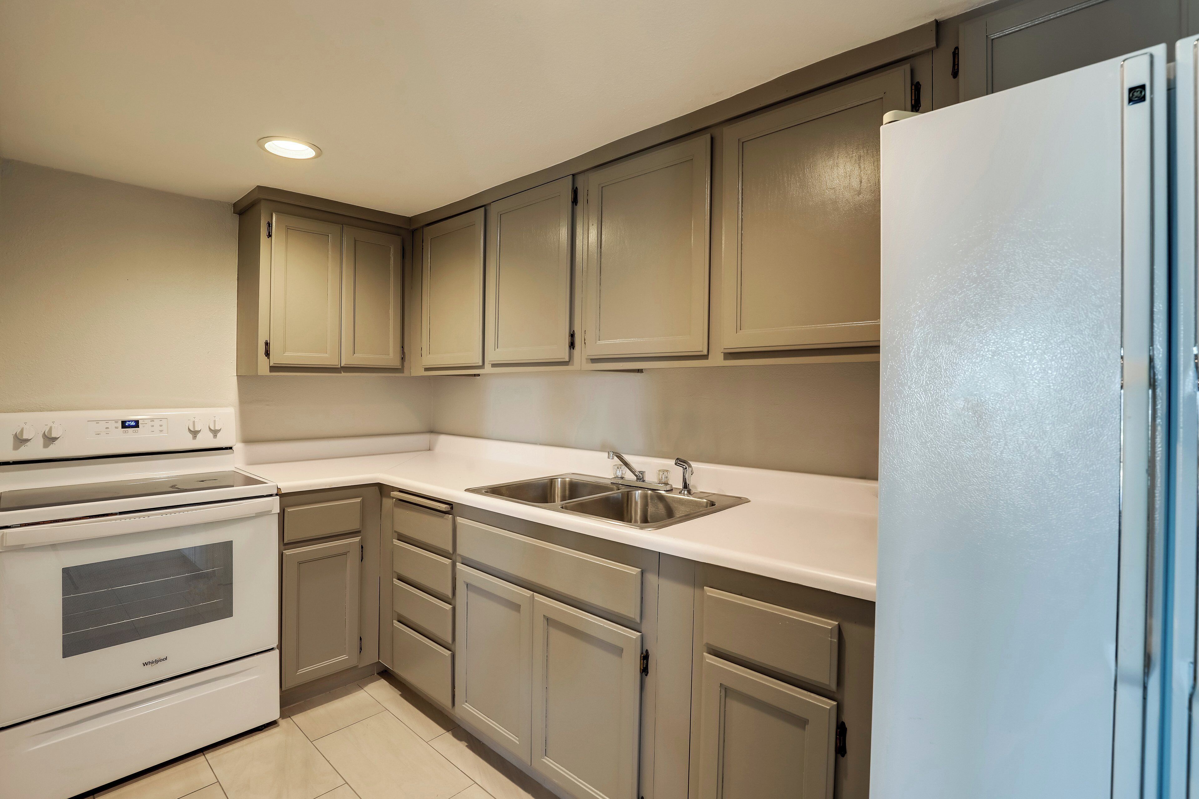 A kitchen with a white stove, sink, and refrigerator, beige cabinets, and a white countertop.