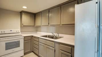 A kitchen with a white stove, sink, and refrigerator, beige cabinets, and a white countertop.