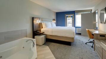 A modern hotel room with a large bed, a separate desk, a bathroom with a bathtub, and a view of the city through the window.